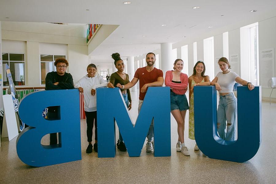 group of students pose by a giant UMB in campus center.